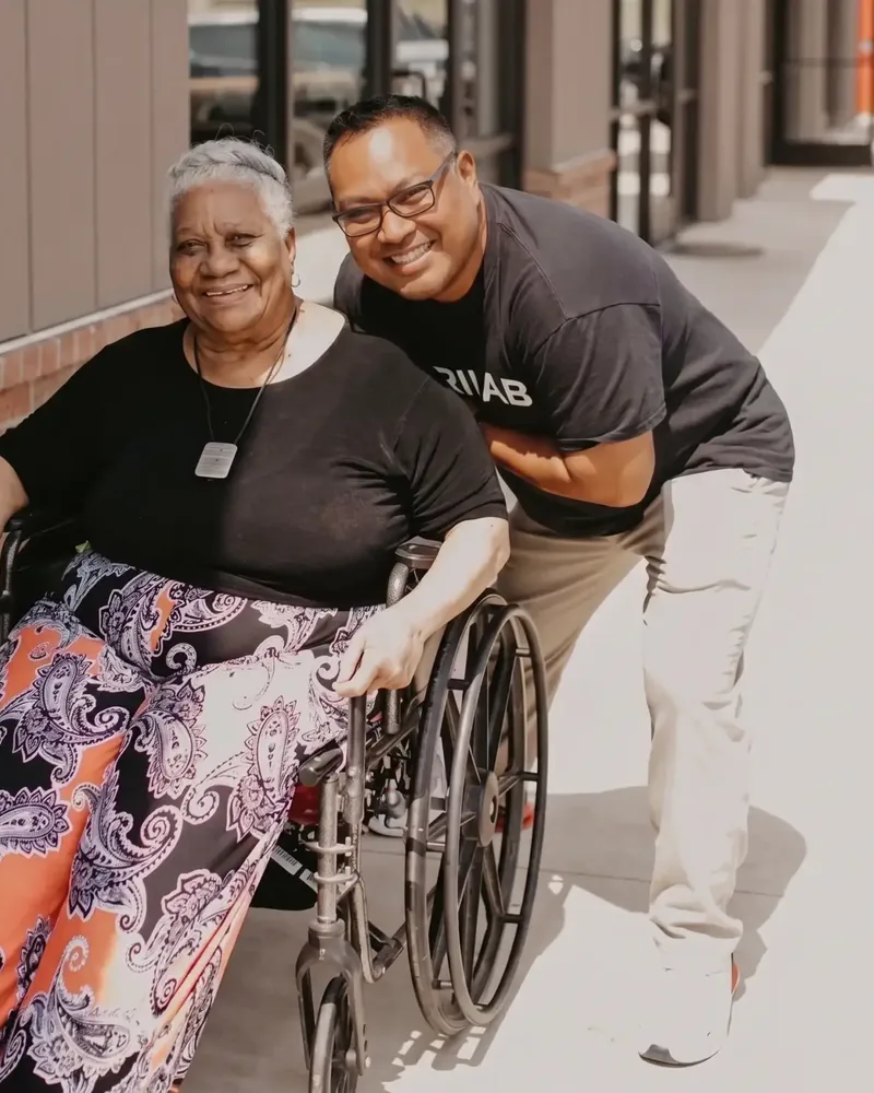 Dr. Michael Chua crouched beside a smiling patient in a wheelchair outside the clinic